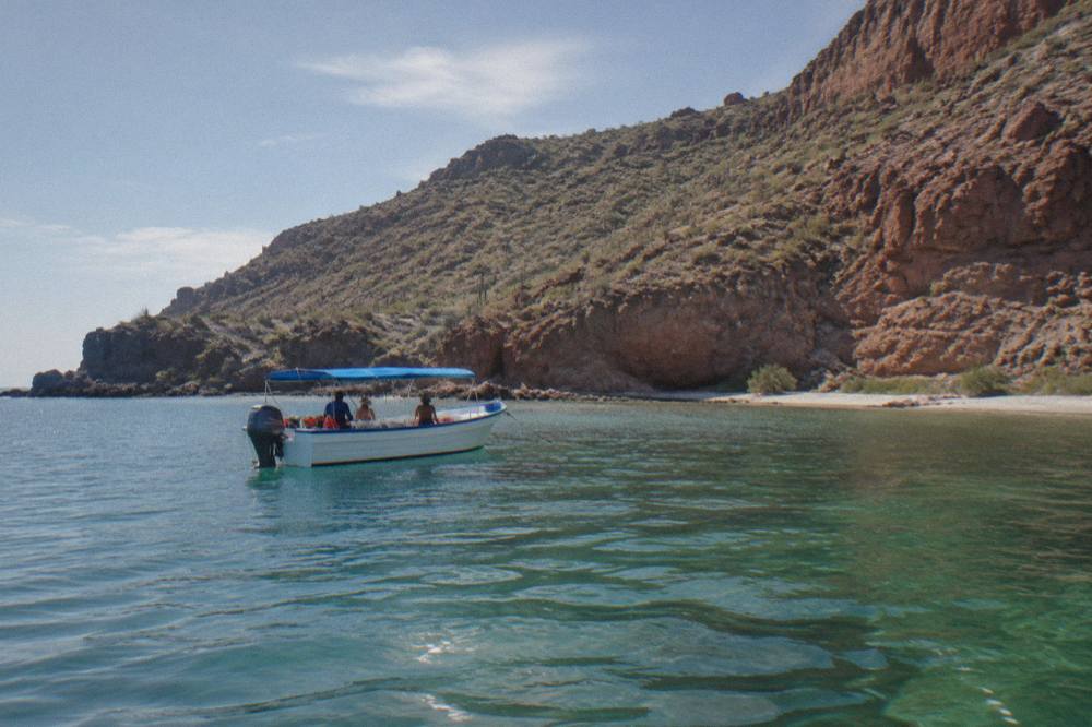 A small snorkel boat anchored on calm green water in a wide bay near La Paz