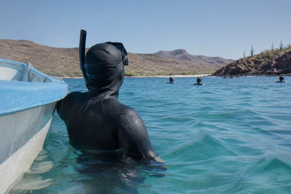 Swimmer in a full wetsuit and snorkel resting upright in clear blue water