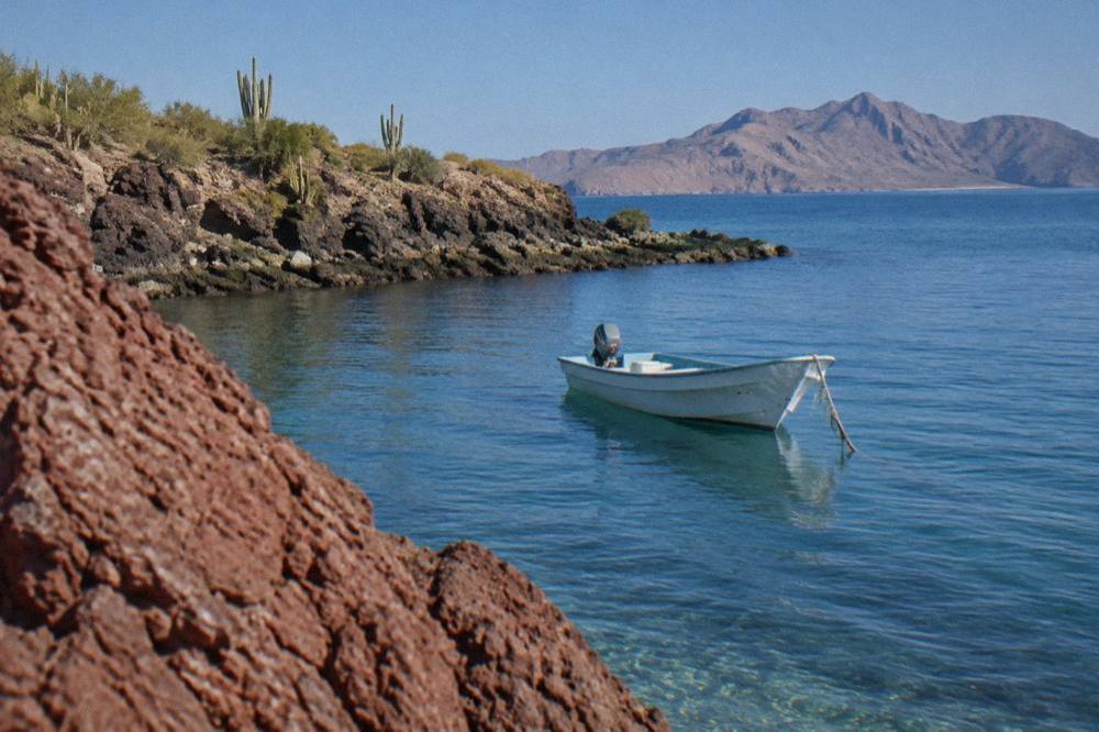 A small open tour boat anchored near a rocky point in a calm blue bay