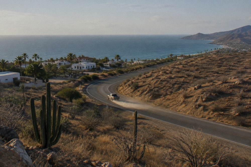 A coastal highway curving between dry golden hills and the blue sea