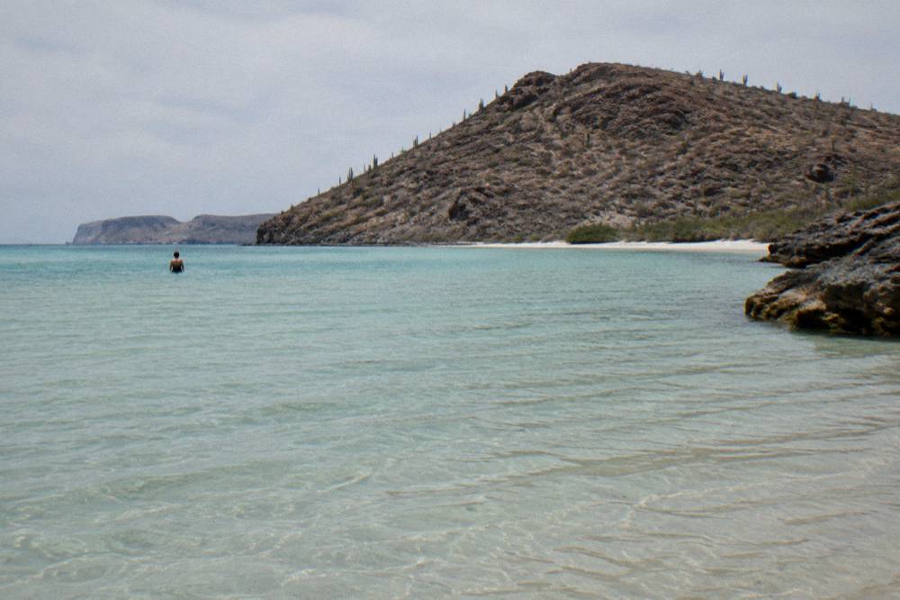 Turquoise shallow water over a white sand beach backed by desert hills