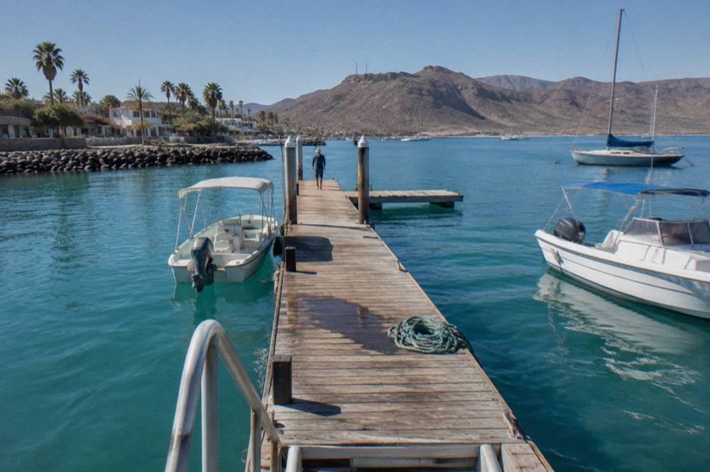 Wooden pier extending into turquoise water near La Paz with hills in the distance