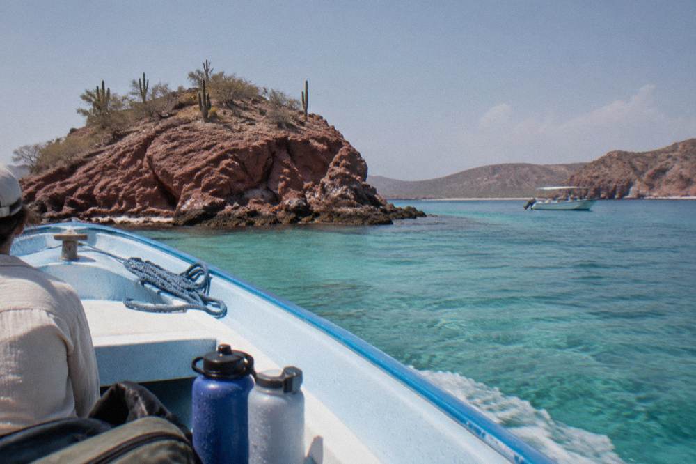 Small boat anchored near rocky islets with clear shallow water along an island shoreline