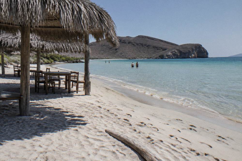 Calm sandy beach with thatched shade structures and clear shallow water near La Paz