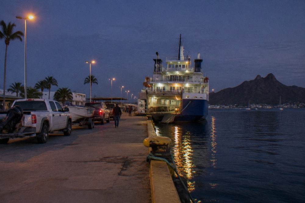 Large ferry vessel tied at a dock at dusk with vehicles waiting on the pier