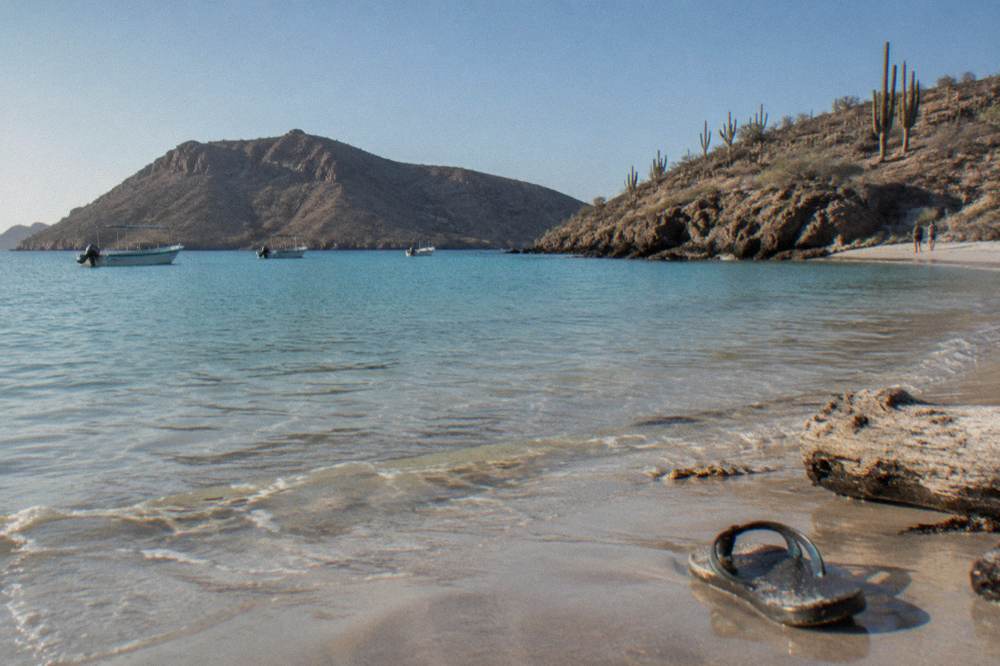 A Protected beach of shallow turquoise water ringed by desert hills at midday