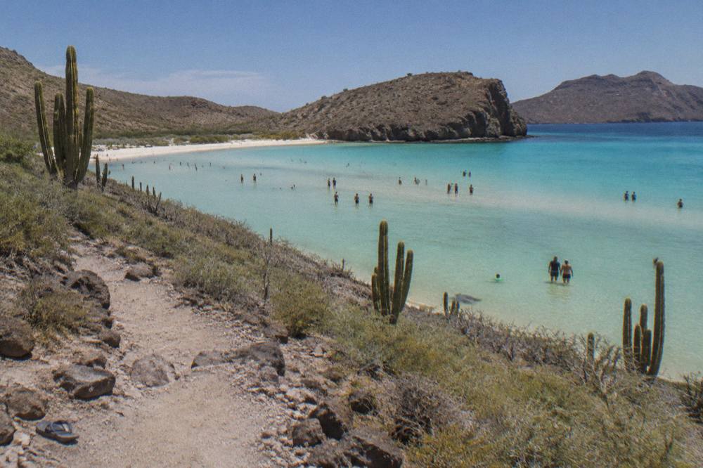 Wide view of a shallow turquoise bay with sandbars and low desert hills behind