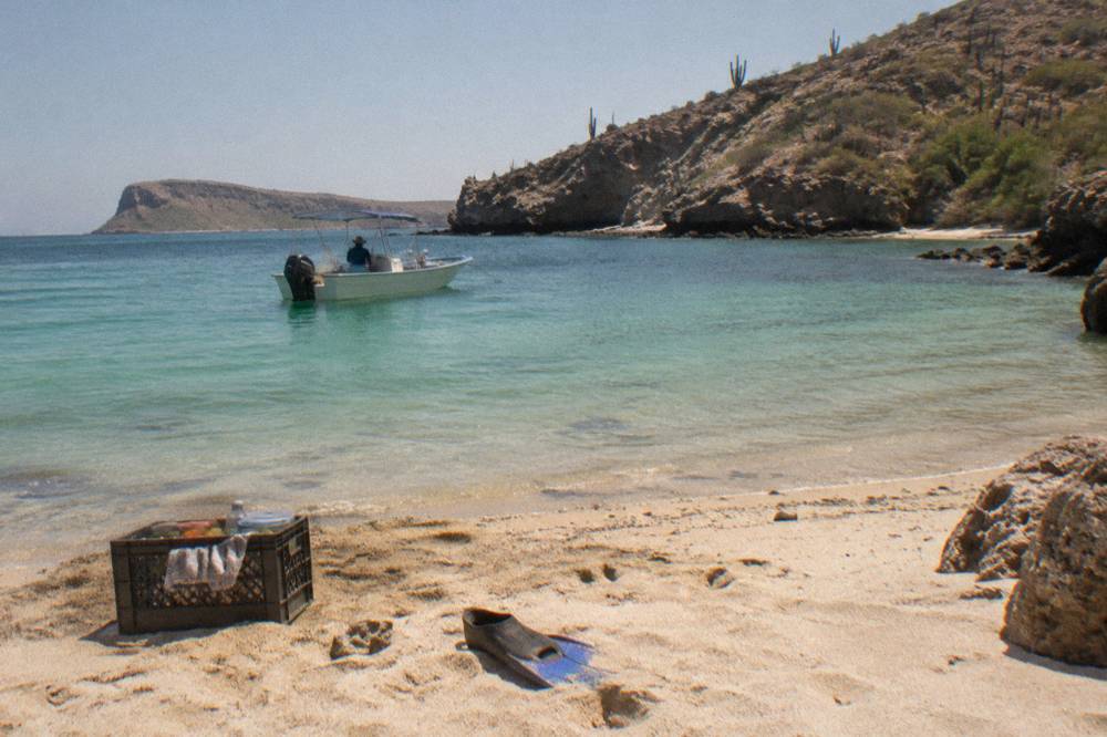 A small boat anchored near a sandy beach beside desert hills at an island bay
