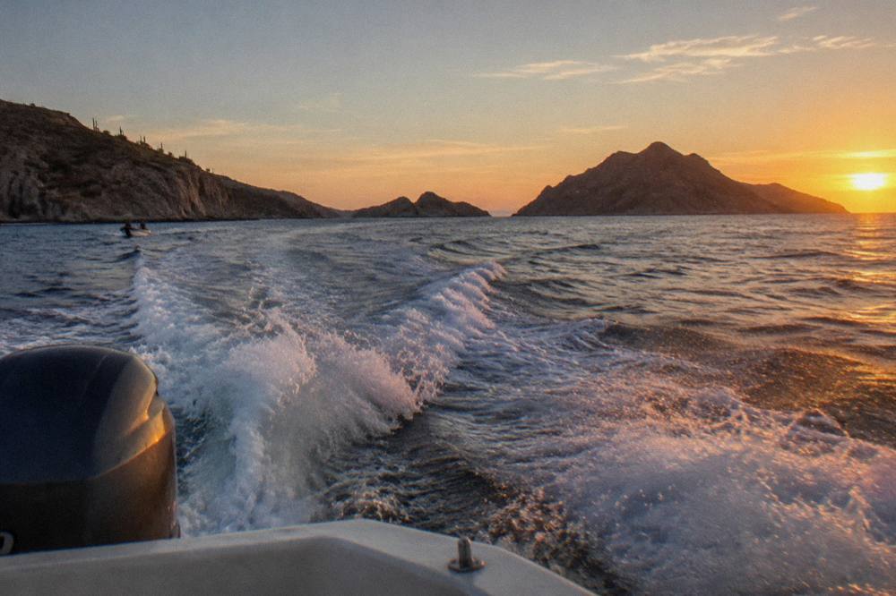 A boat wake crossing open blue water toward desert islands at sunset