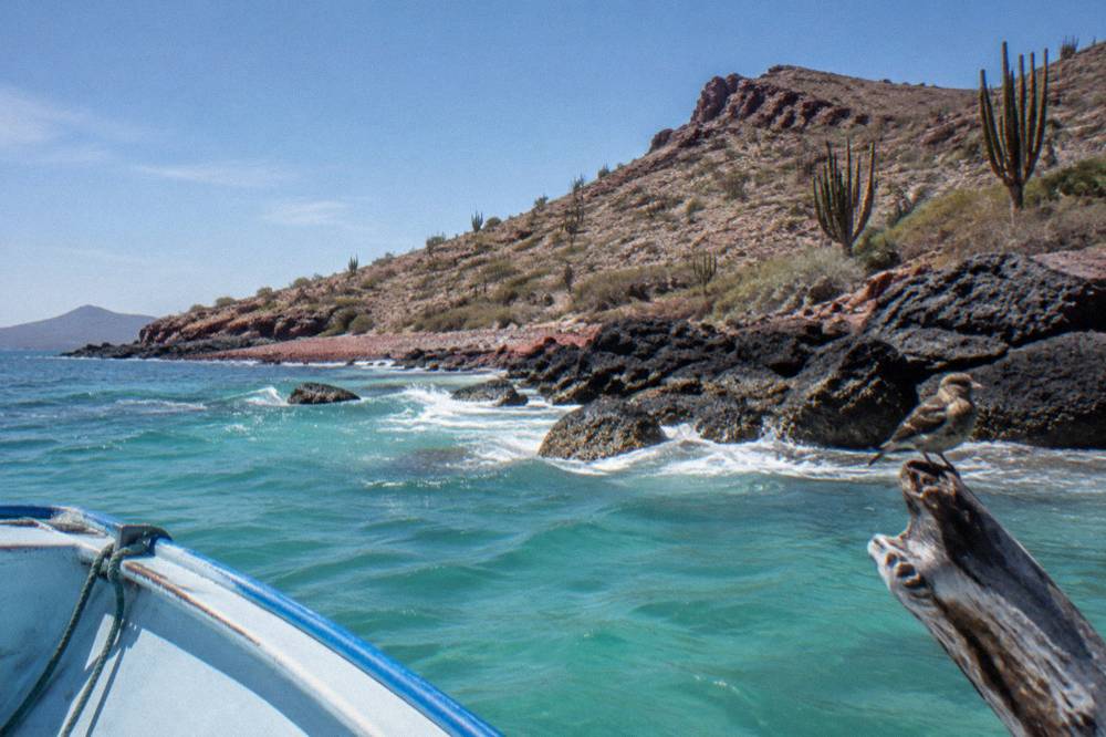 Rocky desert island shoreline with turquoise shallows and a small anchored boat