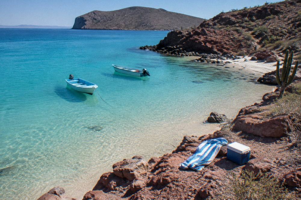 A shallow turquoise cove with a sandy beach and a few small anchored boats