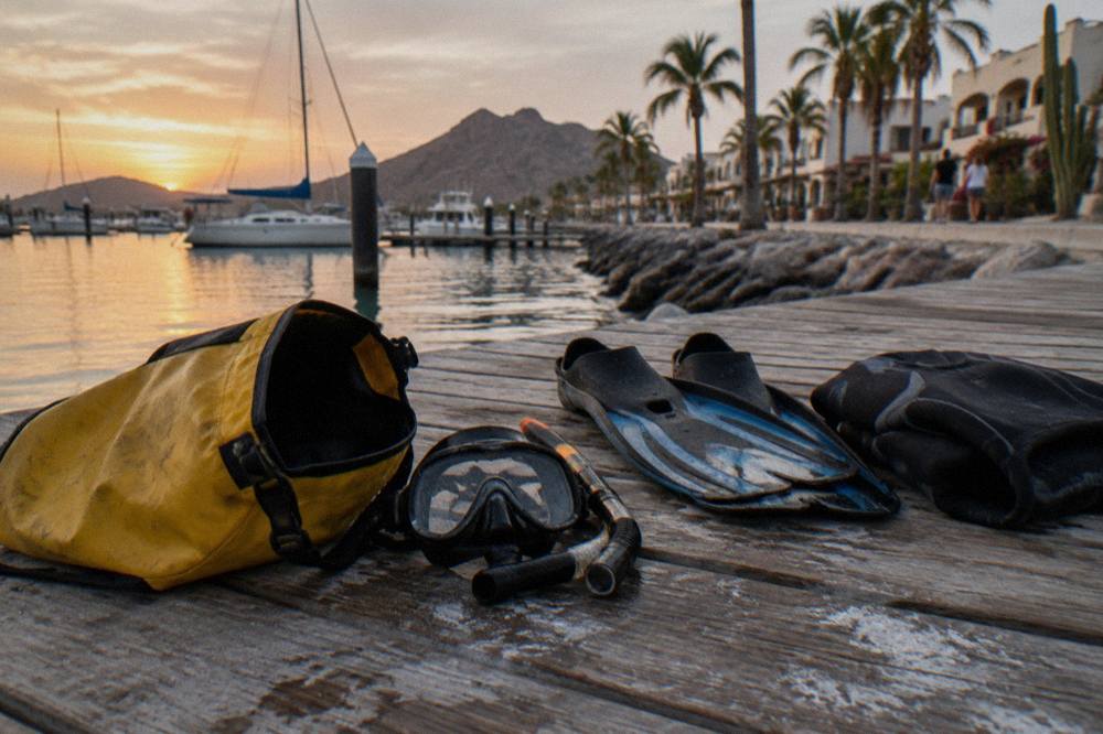 A dry bag with snorkel mask, fins and a folded wetsuit on a wooden dock