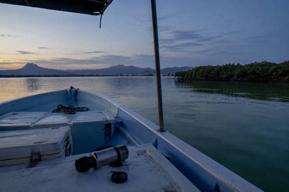 A small boat at anchor on calm green water with a coastline in the distance