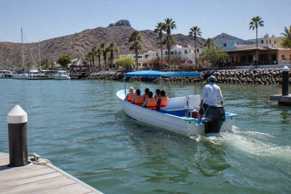 Small motor boat crossing open green water with passengers in life vests and a crew member watching the water
