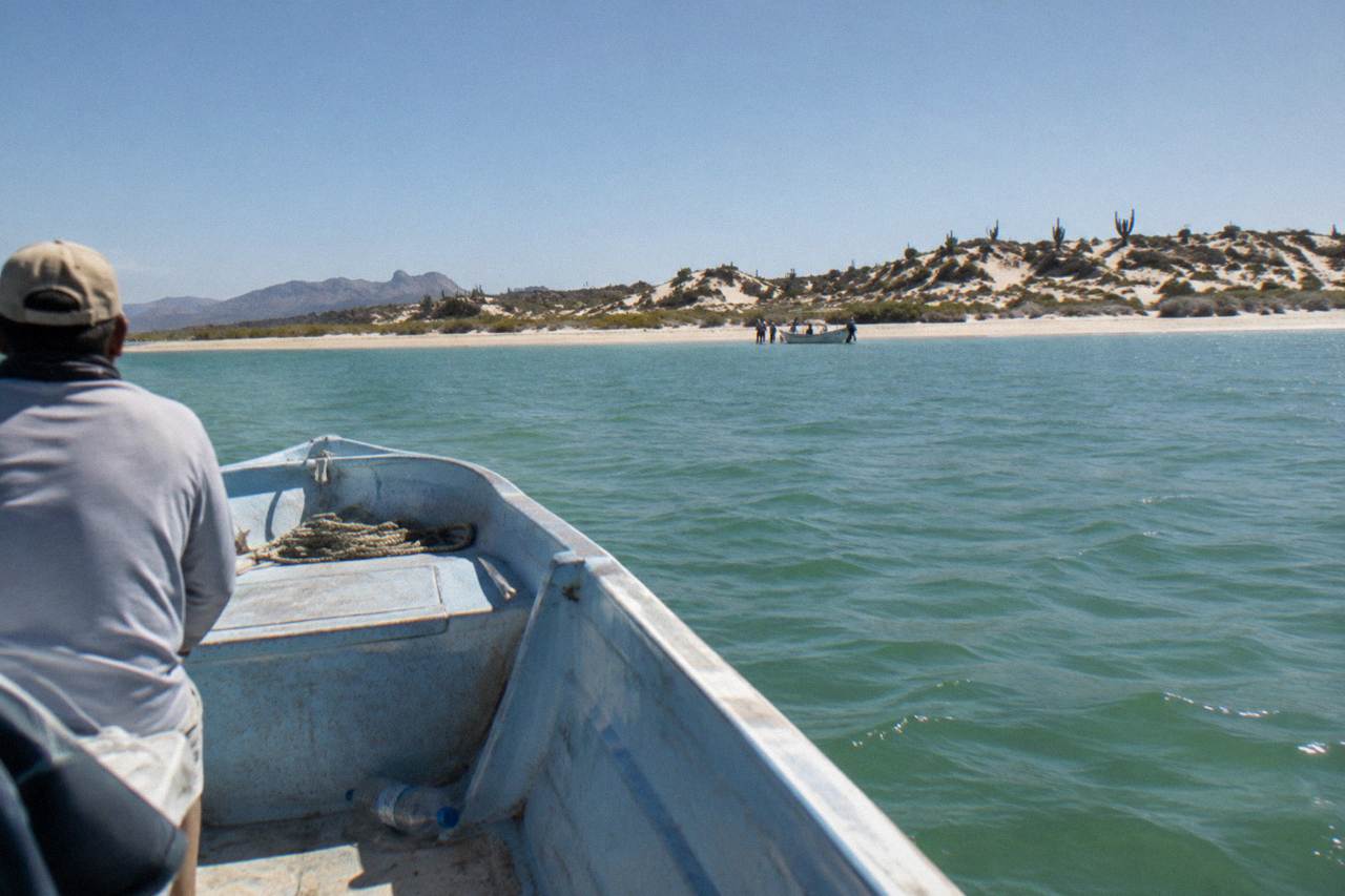 Small boat crossing calm green water in La Paz bay with low hills in the distance