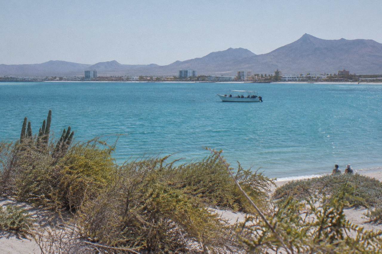 Calm turquoise water of a bay with a small boat and distant hills